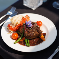 Assiette comprenant un repas bistronomique avec de la viande grillée, une queue de homard, accompagnés de légumes frais du marché