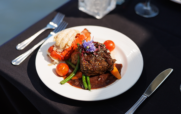 Assiette comprenant un repas bistronomique avec de la viande grillée, une queue de homard, accompagnés de légumes frais du marché