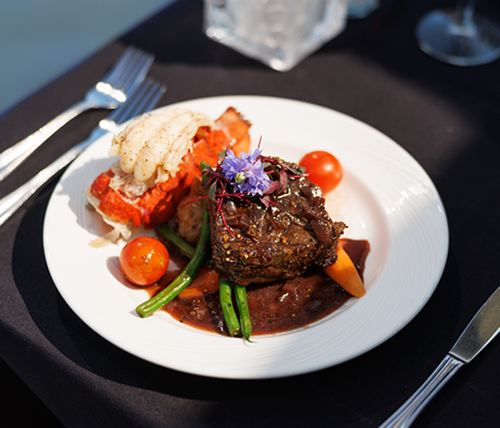 Assiette comprenant un repas bistronomique avec de la viande grillée, une queue de homard, accompagnés de légumes frais du marché