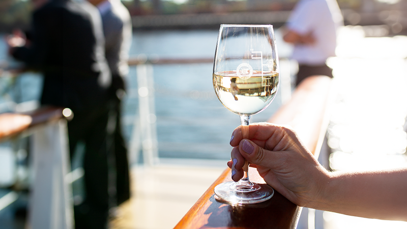 Une main en gros plan tenant un verre de vin blanc sur une des terrasses du navire à Montréal.
