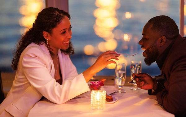 Un couple romantique et souriant dégustant un repas bistronomique avec vue sur les lumières de la ville