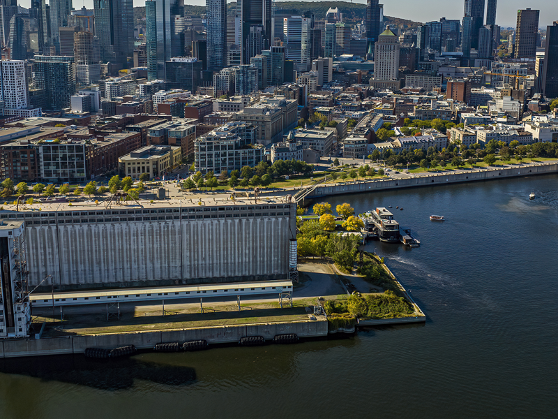 Vue aérienne du navire AML Cavalier Maxim sortant du Vieux Port de Montréal avec une vue sur la ville en arrière plan sous un ciel bleu