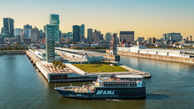 Vue aérienne du navire AML Cavalier Maxim stationné devant la Tour du Port de Montréal de soir avec vue sur la skyline de la ville et le coucher de soleil en arrière plan.