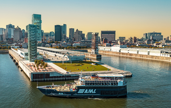 Vue aérienne du navire AML Cavalier Maxim stationné devant la Tour du Port de Montréal de soir avec vue sur la skyline de la ville et le coucher de soleil en arrière plan.