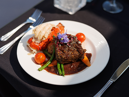 Assiette comprenant un repas bistronomique avec de la viande grillée, une queue de homard, accompagnés de légumes frais du marché