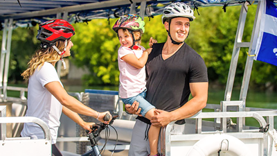 A couple and a child enjoying a ride on a river shuttle on the St. Lawrence River in Montreal. The woman is holding a bicycle and wearing a helmet, while the man is carrying the child in his arms.