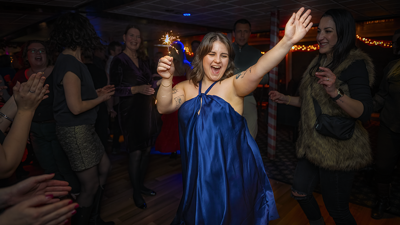Une femme vêtue d'une robe bleue tenant joyeusement un feu de bengale en l'air célébrant Noël entourée d'amis.