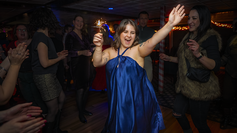 Une femme vêtue d'une robe bleue tenant joyeusement un feu de bengale en l'air célébrant Noël entourée d'amis.
