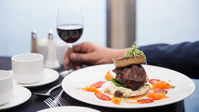 Une assiette de plat bistronomique comprenant un plat de bœuf joliment servi avec des légumes frais du marché, accompagné d'un verre de vin rouge.