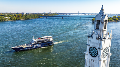 Le navire AML Cavalier Maxim naviguant sur le fleuve Saint-Laurent avec au premier plan la tour de l'horloge de Montréal et en arrière plan l'Ile Sainte Hélène et le Pont Samuel de Champlain
