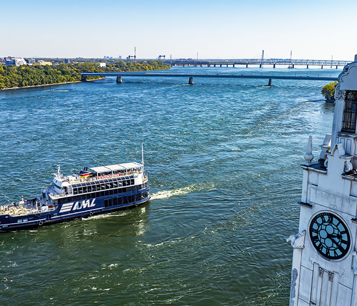Le navire AML Cavalier Maxim naviguant sur le fleuve Saint-Laurent avec au premier plan la tour de l'horloge de Montréal et en arrière plan l'Ile Sainte Hélène et le Pont Samuel de Champlain