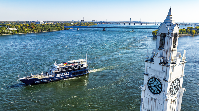 Le navire AML Cavalier Maxim naviguant sur le fleuve Saint-Laurent avec au premier plan la tour de l'horloge de Montréal et en arrière plan l'Ile Sainte Hélène et le Pont Samuel de Champlain