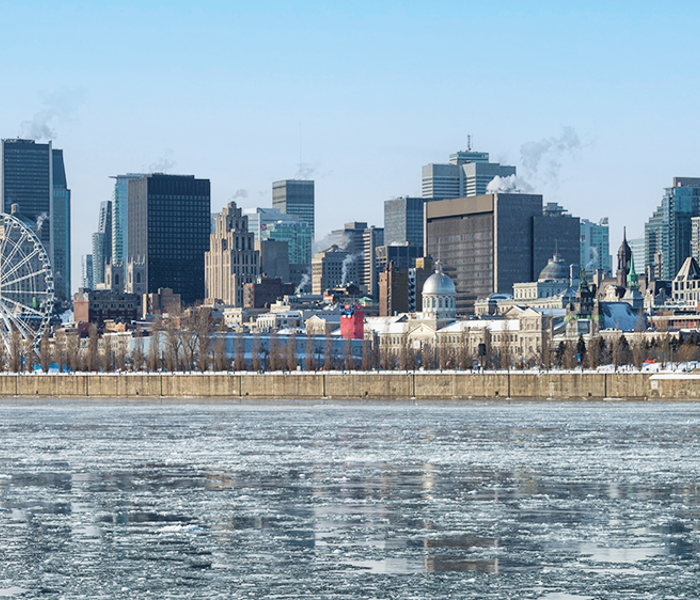 Paysage du Vieux Port de Montréal en hiver avec vue sur la grande roue, le fleuve Saint-Laurent gelé au premier plan et la skyline de la ville en arrière plan.