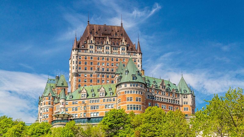 Le Château Frontenac de Québec se dressant majestueusement avec un ciel bleu et de la verdure luxuriante.