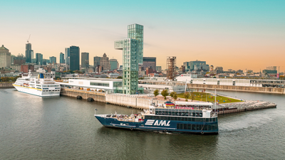 Vue aérienne du navire AML Cavalier Maxim entrant dans le Vieux-Port de Montréal de soir avec vue sur la skyline de la ville en arrière plan.