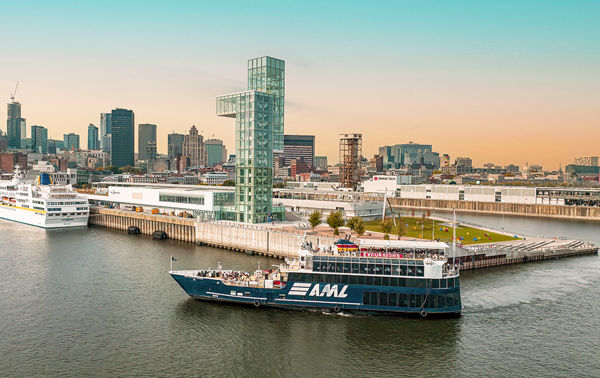 Vue aérienne du navire AML Cavalier Maxim entrant dans le Vieux-Port de Montréal de soir avec vue sur la skyline de la ville en arrière plan.