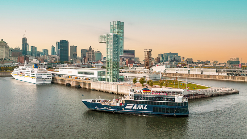 Vue aérienne du navire AML Cavalier Maxim entrant dans le Vieux-Port de Montréal de soir avec vue sur la skyline de la ville en arrière plan.