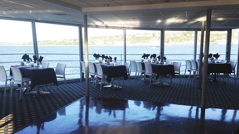 Salle intérieure avec des tables dressées devant une fenêtre donnant vue sur le fleuve Saint-Laurent à Québec