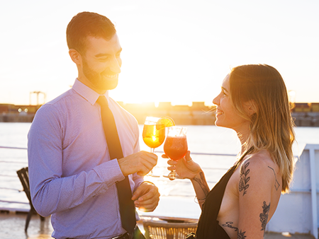 Couple complice et souriant buvant un cocktail sur la terrasse du navire AML Cavalier Maxim à Montréal avec un coucher de soleil en arrière plan