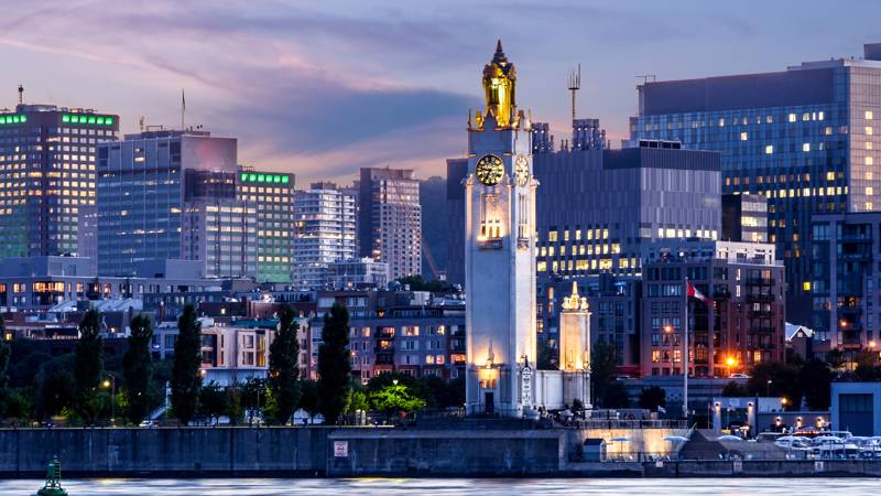 Tour de l'horloge de Montréal de soir en premier plan avec la skyline de Montréal en arrière plan.