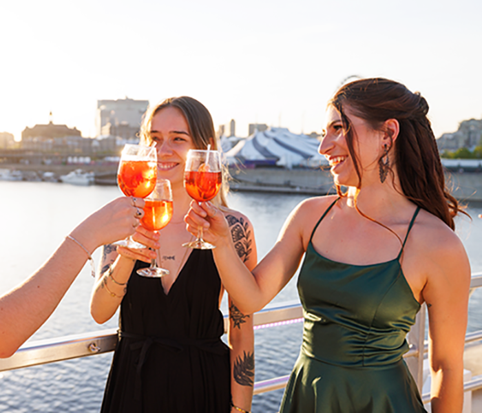 Trois femmes habillées de façon élégante trinquant avec des cocktails sur la terrasse du navire AML Cavalier Maxim à Montréal 