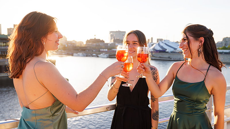 Trois femmes habillées de façon élégante trinquant avec des cocktails sur la terrasse du navire AML Cavalier Maxim à Montréal 