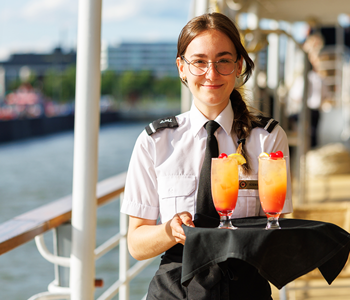 Serveuse tenant un plateau avec des cocktails orangés sur la terrasse extérieure du navire AMl Cavalier Maxim à Montréal. 