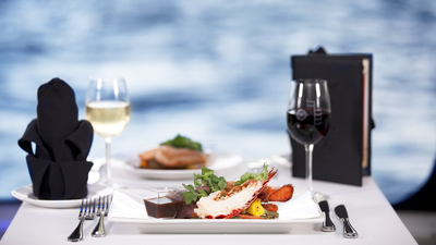 Une assiette de homard, un verre de vin blanc et du vin rouge sur une table avec vue sur le Saint-Laurent à Montréal.