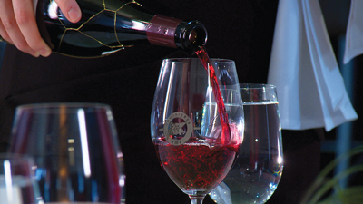 Gros plan sur un serveur qui remplit un verre de vin rouge. 