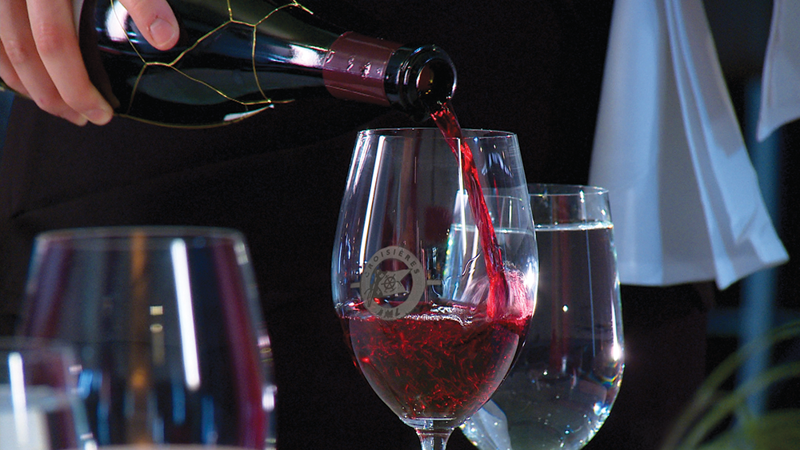 Gros plan sur un serveur qui remplit un verre de vin rouge. 