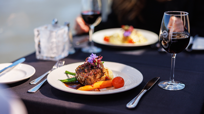 Un plat de steak gourmet garni d'une fleur, accompagné d'un verre de vin rouge, avec vue sur le cadre serein d'une vue sur l'eau.