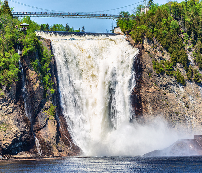 Chute Montmorency en été se jetant dans la rivière Montmorency en contrebas, entourée d'arbres avec une passerelle suspendue au-dessus