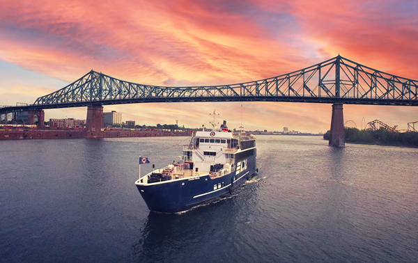 Le navire AML Cavalier Maxim naviguant seul sur le fleuve Saint-Laurent avec le Pont Jacques Cartier et un coucher de soleil vibrant en arrière plan.