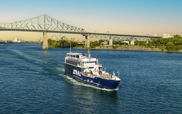 Le navire AML Cavalier Maxim au premier plan naviguant sur le fleuve Saint-Laurent avec une vue sur le Pont Jacques Cartier en arrière plan.