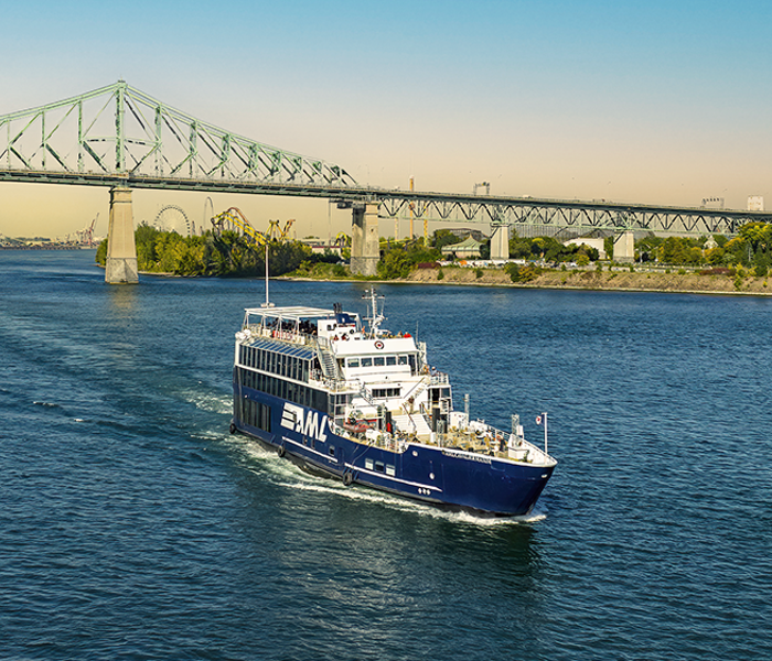Le navire AML Cavalier Maxim au premier plan naviguant sur le fleuve Saint-Laurent avec une vue sur le Pont Jacques Cartier en arrière plan.
