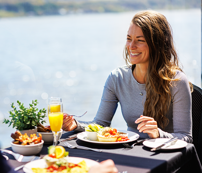 Couple complice dégustant un brunch Signature comprenant des pommes de terre grelots, des œufs, du bacon, et des légumes frais, accompagnées de deux verres de mimosa
