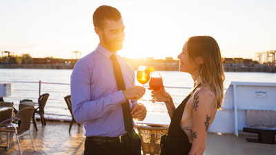 Un homme et une femme prennent un verre ensemble sur l'une des terrasses du navire AML Cavalier Maxim à Montréal en appréciant le coucher de soleil en arrière plan.