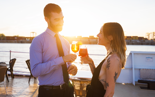Un homme et une femme prennent un verre ensemble sur l'une des terrasses du navire AML Cavalier Maxim à Montréal en appréciant le coucher de soleil en arrière plan.