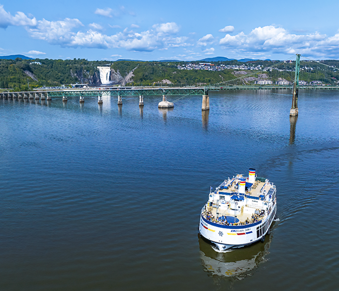Vue aérienne du navire AML Louis Jolliet naviguant sur le fleuve Saint-Laurent avec le pont de l'Île d'Orléans et la Chute Montmorency en arrière plan.