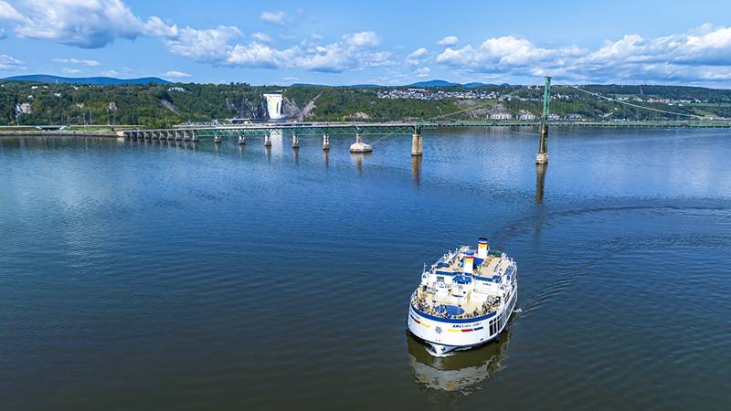 Vue aérienne du navire AML Louis Jolliet naviguant sur le fleuve Saint-Laurent avec le pont de l'Île d'Orléans et la Chute Montmorency en arrière plan.