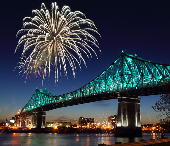 Jacques Cartier Bridge in Montreal at night, illuminated with fireworks overhead, overlooking the monument