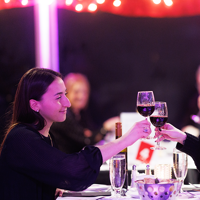 Couple souriant et complice assis à une table trinquant avec un verre de vin rouge avec des décorations de Noël en arrière plan
