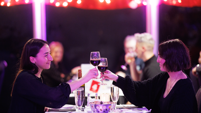 Couple souriant et complice assis à une table trinquant avec un verre de vin rouge avec des décorations de Noël en arrière plan
